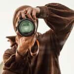 Close-up of a woman in a hijab holding a DSLR camera, capturing a moment.
